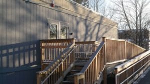 The side of a modular building with wooden stairs and a walkway.