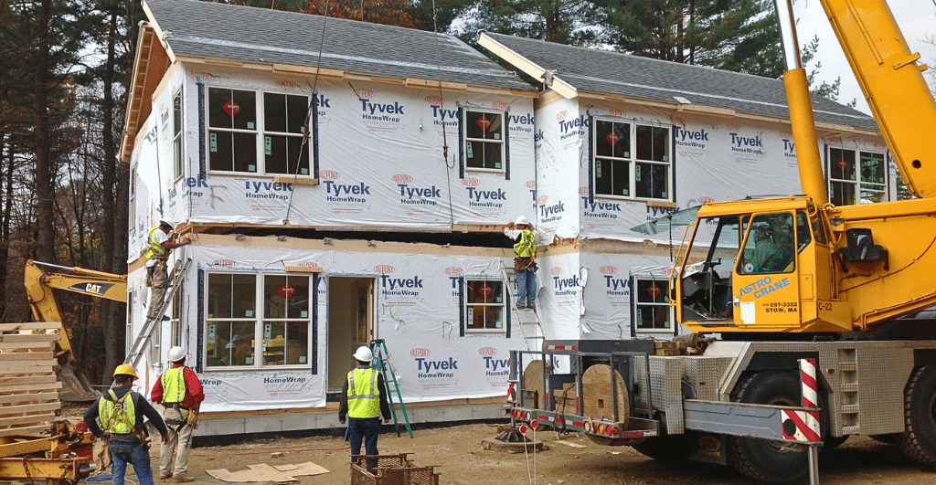 Construction crew installing a two-story modular housing building with a crane, showing off-site-built residential modules being set in place.
